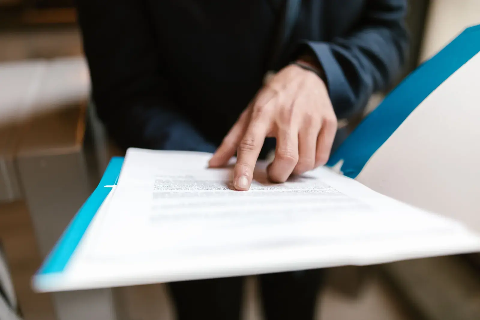 Person pointing to a line of text in a document held in a blue folder